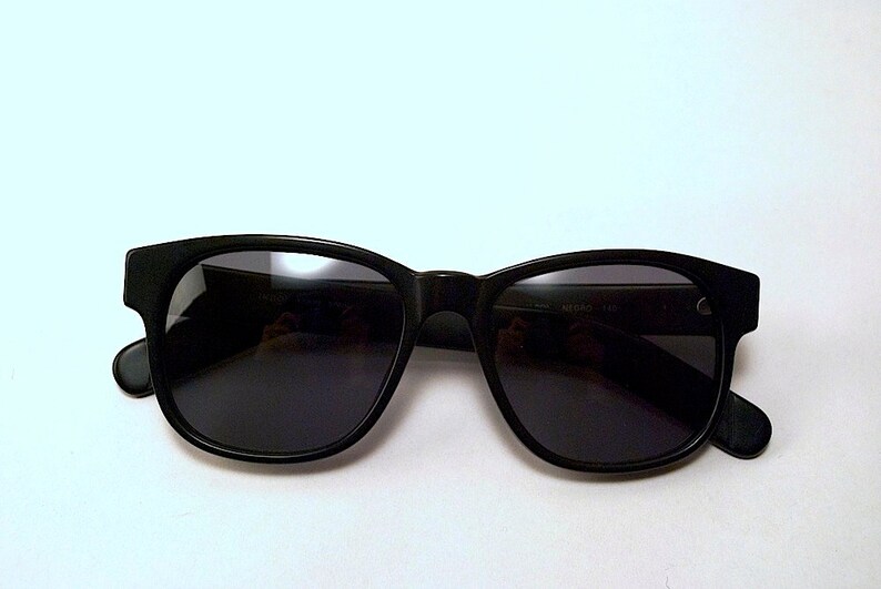 May include: Black plastic sunglasses with dark lenses. The sunglasses have a classic rectangular shape.
