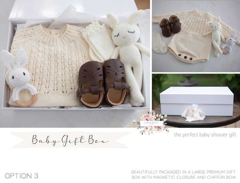 K&ouml;nnte beinhalten: Eine wei&szlig;e Geschenkbox gef&uuml;llt mit Babyartikeln, darunter ein gestrickter Pullover, ein Paar braune Schuhe, ein gestricktes H&auml;schen, eine Rassel und ein Paar Socken. Die Box ist mit einem wei&szlig;en Band verziert und der Text "Baby Gift Box" steht auf der Vorderseite.