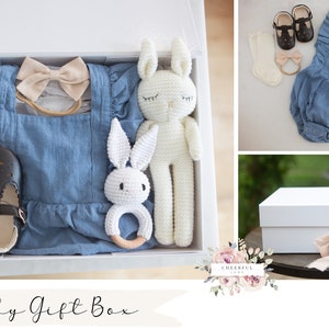 K&ouml;nnte beinhalten: Eine wei&szlig;e Geschenkbox gef&uuml;llt mit Babyartikeln, darunter ein blauer Jeans-Strampler, ein Paar schwarze Schuhe, ein Paar wei&szlig;e Socken, ein beiges Stirnband mit Schleife und zwei wei&szlig;e geh&auml;kelte Hasenspielzeuge. Die Box ist mit "Baby Gift Box" und "OPTION 11" beschriftet.