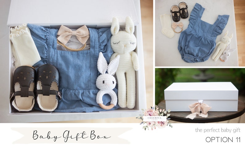 K&ouml;nnte beinhalten: Eine wei&szlig;e Geschenkbox gef&uuml;llt mit Babyartikeln, darunter ein blauer Jeans-Strampler, ein Paar schwarze Schuhe, ein Paar wei&szlig;e Socken, ein beiges Stirnband mit Schleife und zwei wei&szlig;e geh&auml;kelte Hasenspielzeuge. Die Box ist mit "Baby Gift Box" und "OPTION 11" beschriftet.