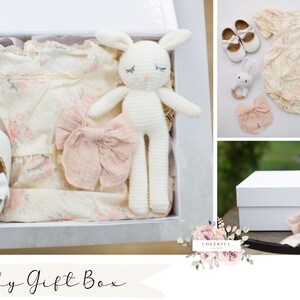 K&ouml;nnte beinhalten: Wei&szlig;e Geschenkbox gef&uuml;llt mit Babyartikeln, darunter ein wei&szlig;er H&auml;kelhase, ein wei&szlig;es Kleid mit Blumenmuster, ein Paar wei&szlig;e Schuhe und eine rosa Schleife. Die Box ist mit "Baby Gift Box" beschriftet.
