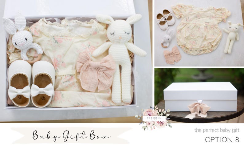 K&ouml;nnte beinhalten: Wei&szlig;e Geschenkbox gef&uuml;llt mit Babyartikeln, darunter ein wei&szlig;er H&auml;kelhase, ein wei&szlig;es Kleid mit Blumenmuster, ein Paar wei&szlig;e Schuhe und eine rosa Schleife. Die Box ist mit "Baby Gift Box" beschriftet.