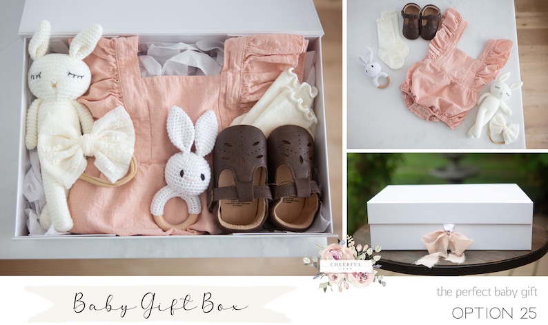 K&ouml;nnte beinhalten: Eine wei&szlig;e Geschenkbox gef&uuml;llt mit einem rosafarbenen Baby-Outfit, einem Paar brauner Schuhe, einem wei&szlig;en H&auml;kel-Hasen, einem Holzring und einem wei&szlig;en Stirnband mit Schleife. Die Box ist mit "Baby Gift Box" und "OPTION 25" beschriftet.