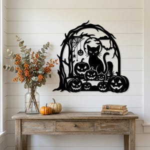 May include: A black metal wall art piece featuring a silhouette of a cat sitting among several jack-o'-lanterns, a spider web, a hanging pumpkin, a full moon, and bare tree branches, all framed within an arched structure.