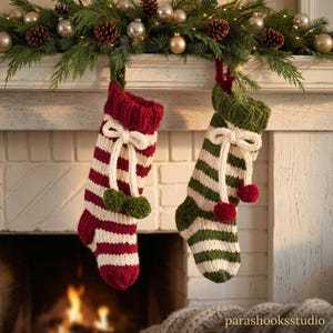 Könnte beinhalten: Zwei gestrickte Weihnachtsstrümpfe hängen nebeneinander. Ein Strumpf hat rote und cremefarbene Querstreifen mit einer cremefarbenen Schleife und zwei grünen Bommeln. Der andere Strumpf hat grüne und cremefarbene Streifen mit einer Schleife und zwei roten Bommeln.