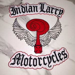 May include: A fabric patch featuring the text Indian Larry in black gothic lettering at the top and Motorcycles in black gothic lettering at the bottom. In the center is a red question mark symbol with white wings and a red cross base.