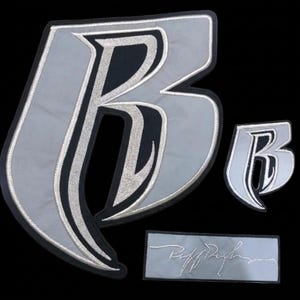 May include: Two embroidered patches featuring a stylised letter B in silver and black, with a larger version on the left and a smaller one on the right. Below them is a rectangular patch with the silver embroidered text Puff Daddy on a grey background.