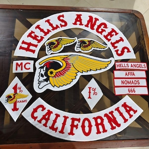 May include: A collection of embroidered patches featuring the text HELLS ANGELS in red on a white background, a large winged skull emblem, two smaller winged skull patches, two diamond-shaped 1% patches, and rectangular patches with text.