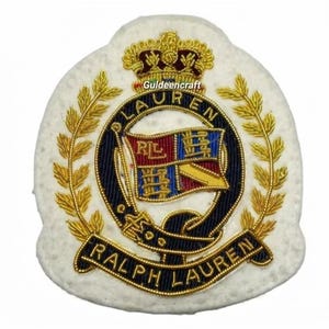 Puede incluir: Un parche bordado blanco con una corona dorada sobre un cinturón circular azul marino con el texto LAUREN. En el interior hay un escudo con secciones rojas, azules y doradas y las letras RL. Hojas de laurel doradas flanquean el diseño con RALPH LAUREN debajo.