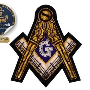 Op de afbeelding: Een maçonniek embleem van een winkelhaak en passer met gedetailleerd gouden borduurwerk op een zwarte achtergrond. Het ontwerp bevat een centraal paars vierkant met een zilveren letter G, omringd door gouden patronen en een zwarte rand.