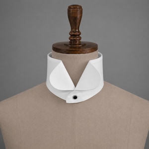 May include: A crisp white detachable shirt collar featuring a high, stiffened band and rounded points. The collar is secured at the front with a single, small, dark-colored button, presenting a clean, structured appearance on a neutral mannequin.