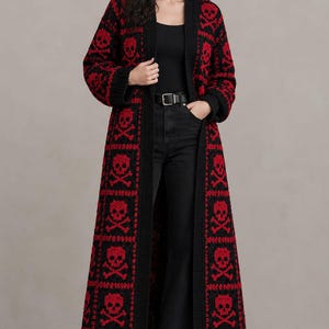 May include: A long, open-front knit cardigan featuring a repeating pattern of red skulls and crossbones on a black background. The garment has long sleeves, a solid black ribbed trim along the front opening, and ribbed cuffs at the wrists.