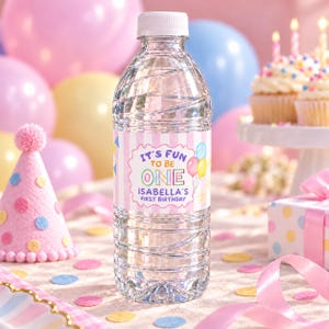 Puede incluir: Una botella de agua de plástico transparente con tapón blanco y una etiqueta personalizada de rayas verticales rosas y blancas. El texto dice: It's fun to be one, Isabella's first birthday, junto a ilustraciones de globos.