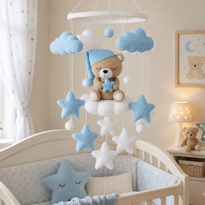 Puede incluir: Un móvil de cuna con un oso de peluche tejido a ganchillo en el centro, que lleva un gorro de dormir azul y sostiene una estrella azul. El móvil incluye varias nubes y estrellas tejidas a ganchillo en tonos azul claro y blanco, suspendidas.