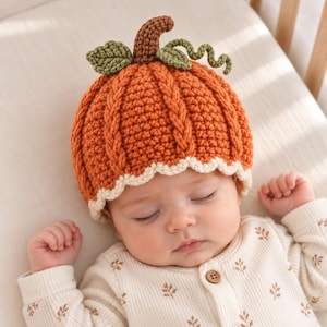 May include: A crochet pumpkin hat featuring a vibrant orange textured body with vertical cable knit patterns, a brown stem, two green leaves, and a curly green vine. The base of the hat is finished with a scalloped cream-coloured border.