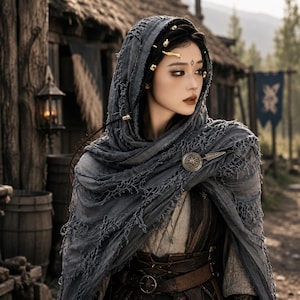 May include: A dark gray distressed fabric hood draped over the head and shoulders, secured with a circular metallic brooch. The hood features frayed edges and is worn over a light-colored garment with a brown leather belt featuring a metal buckle.