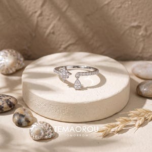 May include: A silver-toned open ring featuring a star-shaped charm set with small clear stones on one end and a single pear-shaped clear stone drop on the other. The band is encrusted with a row of small clear stones along the outer edge.