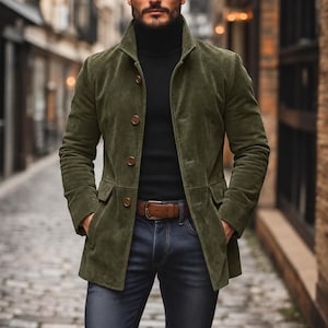 Könnte beinhalten: Eine olivgrüne Wildlederjacke mit hohem Kragen und vier braunen Knöpfen auf der Vorderseite. Die Jacke verfügt über zwei Pattentaschen an der Taille und wird über einem schwarzen Rollkragenpullover getragen, kombiniert mit einer dunkelblauen Jeans.