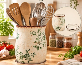 May include: A ceramic utensil holder with a scalloped rim and a matching saucer, featuring a green floral pattern on a cream background. The holder is filled with various wooden and metal kitchen utensils, including a whisk and spatula.