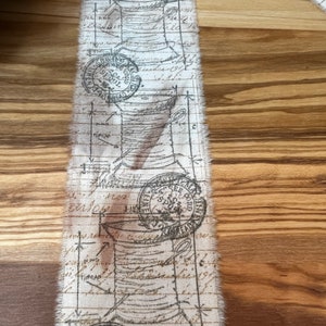 May include: White fabric ribbon with a repeating pattern of brown ink stamps and handwritten text. The stamps feature a circular design with the words "Spool Cotton" and "New York".