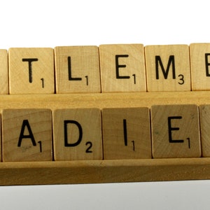 May include: Wooden tiles spelling out the words "GENTLEMEN" and "LADIES" on a wooden rack. The tiles are from a Scrabble game.
