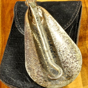 May include: A vintage metal shoe horn with a black leather case. The shoe horn is tarnished and has a worn finish. The case has a flap that closes with a snap.