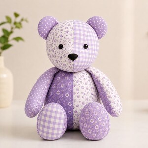 Puede incluir: Un oso de peluche hecho de varios parches de tela lavanda y blanca. El oso presenta un dise&ntilde;o de patr&oacute;n dividido con estampados florales, cuadros vichy y lunares. Tiene dos orejas redondas, una nariz negra y dos ojos negros de cuentas.