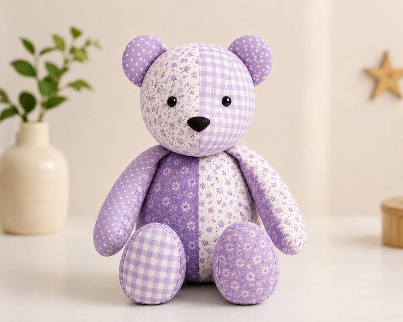 Puede incluir: Un oso de peluche hecho de varios parches de tela lavanda y blanca. El oso presenta un dise&ntilde;o de patr&oacute;n dividido con estampados florales, cuadros vichy y lunares. Tiene dos orejas redondas, una nariz negra y dos ojos negros de cuentas.