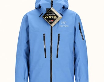 May include: A light blue hooded jacket with a full-length black front zipper, two vertical chest pockets with black zippers, and a smaller zippered pocket on the left sleeve. A Gore-Tex tag hangs from the collar, and the Arc'teryx logo is on the chest.