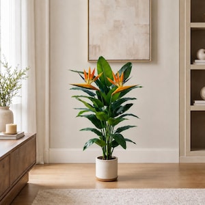 May include: A tall artificial bird of paradise plant with large, dark green leaves and two vibrant orange and blue flowers. The plant is housed in a cylindrical white ceramic pot with a light brown wooden base, standing upright on a floor.