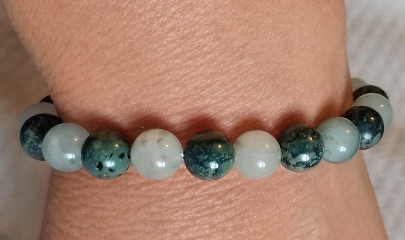 Puede incluir: Una pulsera de cuentas con esferas alternas en tonos verde bosque oscuro con motas negras y cuentas lisas y transl&uacute;cidas de color blanco p&aacute;lido o verde menta claro. Las cuentas est&aacute;n ensartadas en un patr&oacute;n repetitivo sobre un cord&oacute;n el&aacute;stico.