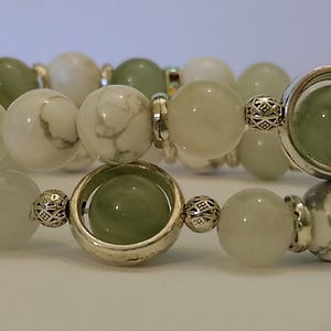 Puede incluir: Una pulsera de varias vueltas con cuentas lisas de mármol blanco y gris intercaladas con cuentas de color verde pálido translúcido. El diseño incluye espaciadores de metal plateado y dos marcos circulares plateados, cada uno con una cuenta verde.