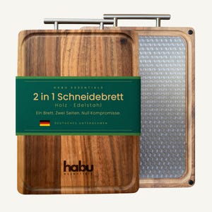 Könnte beinhalten: Ein rechteckiges Schneidebrett aus Holz mit Edelstahlgriff und einer wendbaren Seite aus Metall mit geometrischem Würfelmuster. Ein grünes Papierband umschließt das Brett mit dem Text Habu Essentials 2 in 1 Schneidebrett. Holz · Edelstahl.