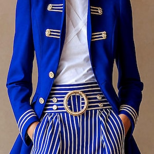May include: A vibrant royal blue blazer with gold-tone military-style buttons and striped collar detailing, worn over a white shirt with a crisscross neckline. The outfit includes high-waisted blue and white striped trousers with a large gold buckle.