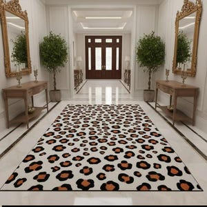 May include: A rectangular area rug featuring a repeating leopard print pattern with black and brown spots on a white background. The rug is positioned centrally on a white marble floor in a hallway, flanked by two wooden console tables and mirrors.