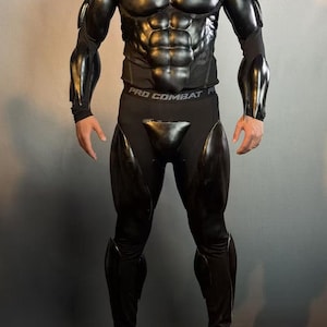 May include: A black full-body suit featuring molded, glossy muscle-shaped armor plates on the chest, shoulders, arms, thighs, and shins. The garment includes a black base layer with a waistband clearly labeled with the text PRO COMBAT.