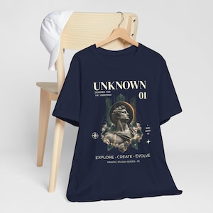 Könnte beinhalten: Ein marineblaues T-Shirt mit einem Grafikdruck einer klassischen Statuenbüste, umgeben von Wolken und einem kreisförmigen Heiligenschein. Der Text lautet UNKNOWN, DESIGNED FOR THE UNDEFINED, 01, EXPLORE CREATE EVOLVE und PRINTX / STUDIO SERIES 01.