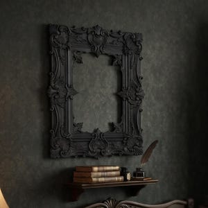 May include: A bedroom scene featuring a dark ornate picture frame mounted on a wall above a wooden headboard. A bedside table holds a lamp, books, and glasses. A bed is dressed in dark bedding with a maroon velvet pillow and a thick knit blanket.
