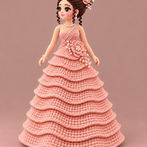 May include: A handcrafted crochet doll featuring dark brown hair styled in an updo with a pink flower accessory. The doll wears a strapless, tiered, light pink gown adorned with a large floral embellishment and pearl accents on the bodice and hair.