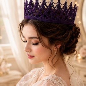 May include: A deep purple crown featuring an intricate, openwork crochet pattern with a pointed, scalloped top edge. The crown has a solid, wide base band and a delicate, web-like structure that rises to form distinct, symmetrical peaks.