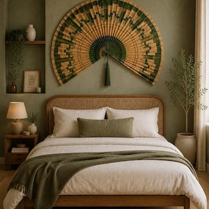 Puede incluir: Un gran abanico de pared semicircular con un patrón geométrico en tonos verde oscuro y bronceado natural, acentuado con una borla central de color verde oscuro. El abanico está montado sobre una cama de madera con cabecero de rejilla.