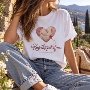 Peut inclure: Un t-shirt blanc à manches courtes orné d'un motif de cœur cousu dans des tons rose et beige. Sous le cœur, le texte "Keep this part of me." et "unfinished by design" est inscrit dans une police cursive et sans-serif rouge foncé.