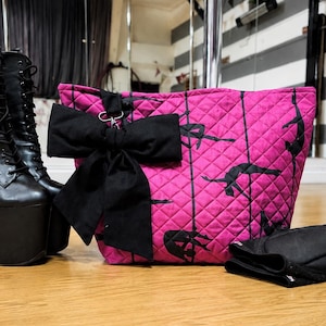 Può includere: Una borsa tote trapuntata rosa acceso con un motivo di sagome di ballerini alla sbarra e linee verticali nere. La borsa è decorata con un grande fiocco in tessuto nero rimovibile fissato con una clip in metallo argentato sulla parte anteriore.