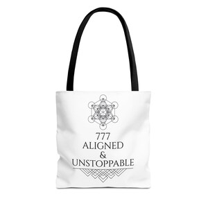 May include: A white tote bag with black handles featuring a black geometric Metatron's cube symbol above the text 777 ALIGNED & UNSTOPPABLE, with a decorative linear pattern underneath the text, all printed in a clean, centered black font.