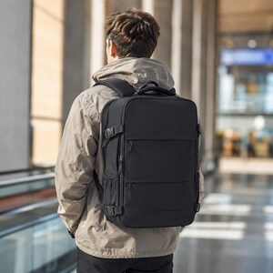 May include: A black rectangular backpack with multiple zippered compartments, side compression straps with plastic buckles, and padded shoulder straps. The bag features a structured design with a flat front panel and side mesh pockets for storage.