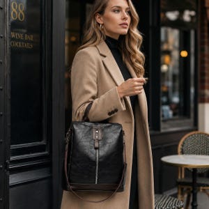 Peut inclure: Un sac à dos en similicuir noir avec une fermeture éclair verticale argentée, une poignée supérieure et des garnitures marron foncé. Le sac présente une sangle centrale avec une fermeture à pression métallique et des bretelles réglables.