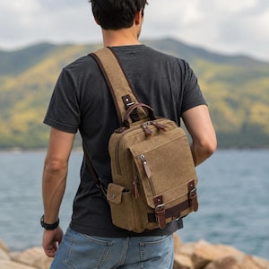 Puede incluir: Una mochila bandolera de lona color caqui con una sola correa para el hombro, múltiples compartimentos con cremallera, detalles en imitación cuero marrón y hebillas metálicas. La bolsa tiene una forma rectangular estructurada.