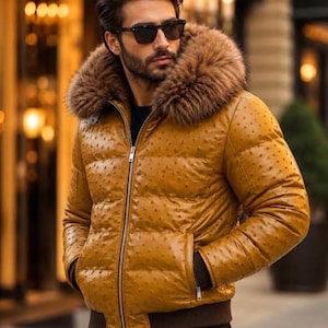 May include: A mustard yellow puffer jacket with a textured ostrich-like finish, featuring a large brown faux fur hood trim, a silver front zipper, and dark brown ribbed cuffs and hem. The jacket has a quilted design and two side pockets.