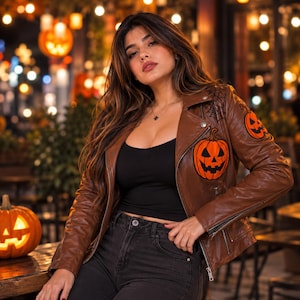 Puede incluir: Una chaqueta de cuero marrón para motocicleta con gráficos de calabazas de Halloween naranjas en el pecho y la manga, acentuada con detalles de telarañas negras en el hombro, sobre una camiseta negra y vaqueros oscuros.