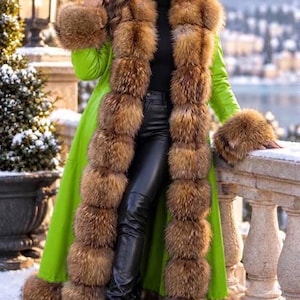 May include: A long, bright lime green coat featuring thick, fluffy brown fur trim along the front opening, cuffs, and hem. The coat is worn over a black turtleneck sweater and black leather trousers, paired with black high-heeled leather boots.